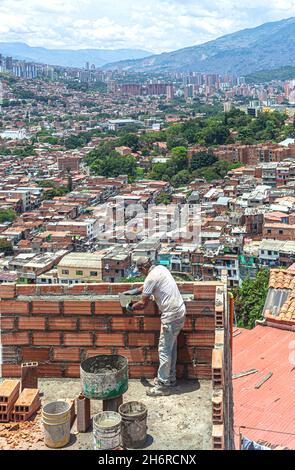 Bricklayer at work on top of a house overlooking the city, Comuna 13, Medellin, Colombia. Stock Photo