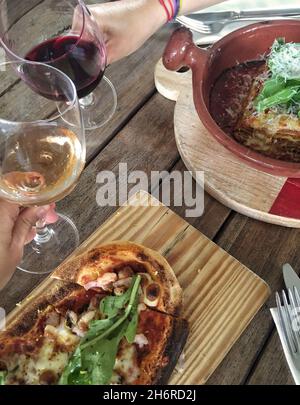 Hands toasting wine glasses against table with pizza in an Italian restaurant Stock Photo