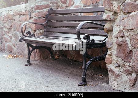 A view of original wooden bench on metal base in front of stone fence on city street Stock Photo