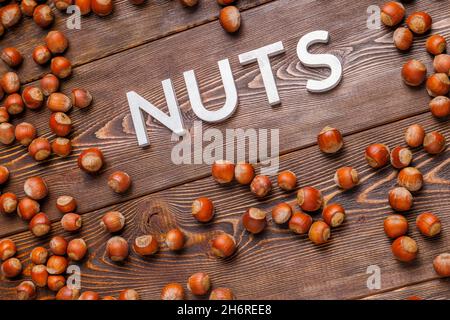 the word nuts laid with silver letters on wooden board background surrounded with scattered hazelnuts Stock Photo