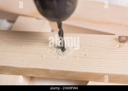Metal drill bit makes a hole for screw in wooden plank in carpenters workshop. Close up, selective focus, and copy space Stock Photo