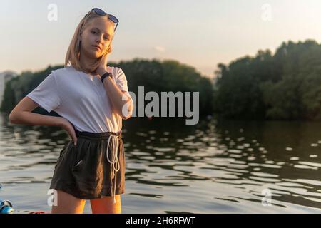 blonde teen girl standing on the lake at sunset. Stock Photo