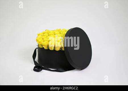 Black round gift flower packaging box with yellow roses inside and opened lid. Stylish flower arrangement. Stock Photo