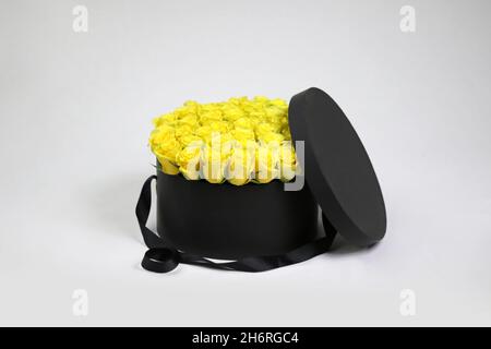 Black round gift flower packaging box with yellow roses inside and opened lid. Stylish flower arrangement. Stock Photo