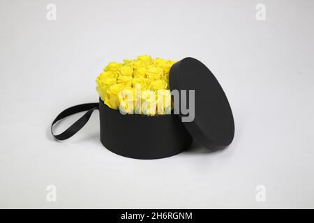 Black round gift flower packaging box with yellow roses inside and opened lid. Stylish flower arrangement. Stock Photo