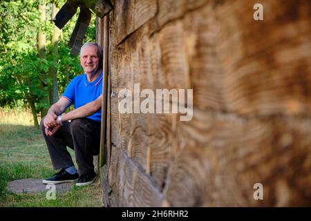 an elderly man sits on the threshold of a wooden hut looking into the distance Stock Photo