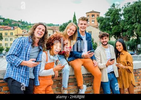Multiethnic teenagers friends smiling and joking using smartphone outdoors - Concept of tecnology and friendship Stock Photo