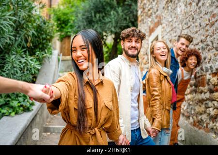 Multiethnic group of teenagers walking in the city holding hands - Young people smiling and running down an alley stairs Stock Photo