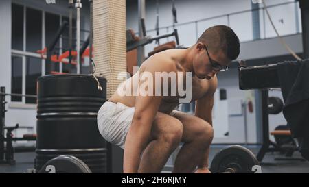 An Arab man squats in the gym with a barbell. Stock Photo