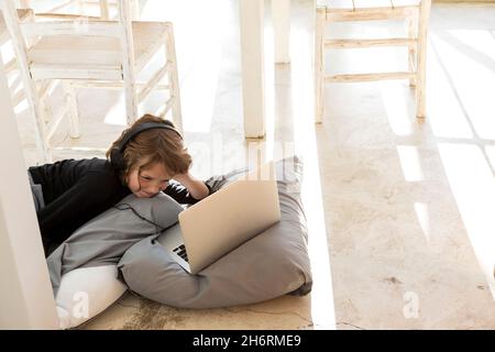 Eight year old boy lying on the floor on cushions using a laptop Stock Photo