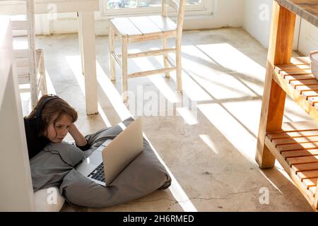 Eight year old boy lying on the floor on cushions using a laptop Stock Photo