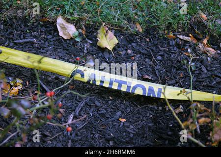 The yellow Caution tape laying on the ground with the soil and the grass with spare leaves Stock Photo