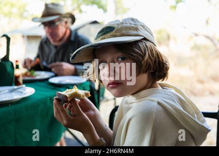 Young boy eating a piece of toast at a table in a safari camp Stock Photo