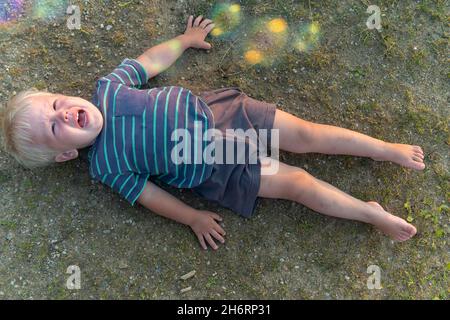 a little boy lies on the ground and cries a lot. resentment or hysteria in a child. Stock Photo