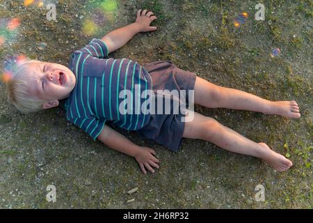 a little boy lies on the ground and cries a lot. resentment or hysteria in a child. Stock Photo