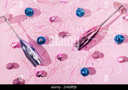 Two shiny metallic Champagne glasses, blue and pink, blue disco balls, pink Christmas balls and holographic tinsels on pastel pink background. Romanti Stock Photo