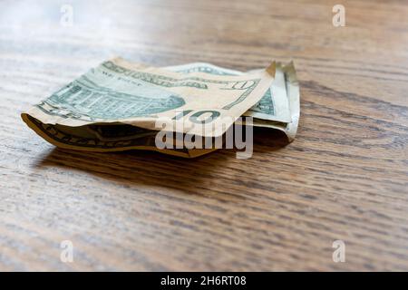 $10 and $1 of US money sits folded on a wooden table. Stock Photo
