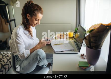 Woman sitting at the desk, looking at her phone and smiling. Stock Photo