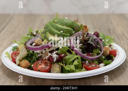 Mixed greens house salad piled high on the plate with healthy vegetables, onions, and avocado slices. Stock Photo