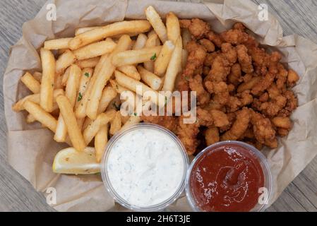 Overhead view of combination basket full of deep fried clams and a side of french fries with ketchup and dipping sauce. Stock Photo