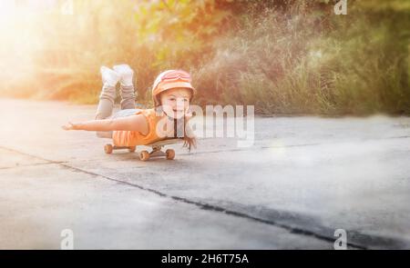 Happy child lies on a skateboard and rides cheerfully along the road ahead Stock Photo