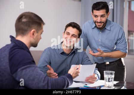 Three smiling men discussing papers at desk Stock Photo
