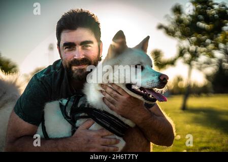 Portrait of a smiling adult Argentinian man posing with his Akita dog in a park Stock Photo