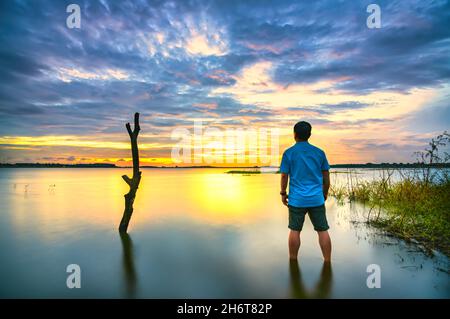 Silhouette traveler man watching sunset sky at hydroelectric lake after a trip back home in Dong Nai, Vietnam Stock Photo
