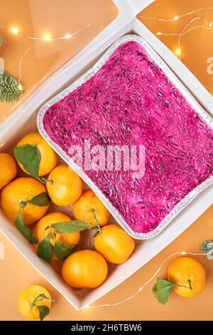 Russian traditional salad, dressed herring under fur coat in take way box. Menu food for delivery in the Coronavirus Pandemic. Tangerines and branches Stock Photo