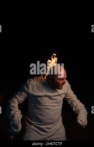 Bald man in a straitjacket with a burning head on a dark background. Stock Photo