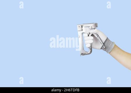 Gloved hands holding stapler construction tools. Work tools on blue background Stock Photo