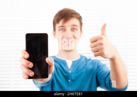 Happy Young Man show a Screen of the Mobile Phone and Thumb Up Gesture Stock Photo