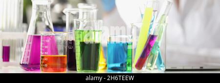 Multi-colored liquid in flasks in background woman scientist looks through microscope Stock Photo