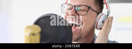 Portrait of singing young man in headphones front of microphone in studio Stock Photo