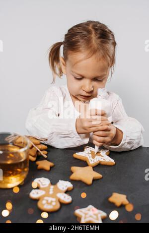 Child cooking and eating home made gingerbread cookies, stars, man. Happy toddler girl celebrated Christmas eve at home, Kid decorating pastry with Stock Photo