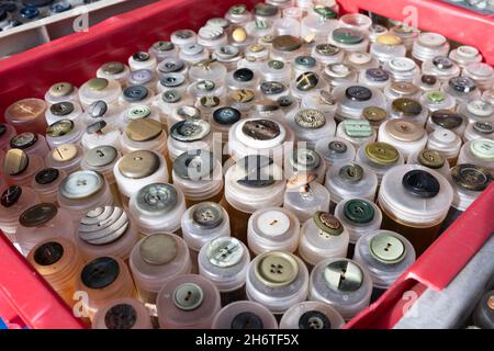 Buttons in all shapes, materials, sizes and colors in plastic tubes in a market stall. Focus on the buttons at the bottom, in the front of the box Stock Photo