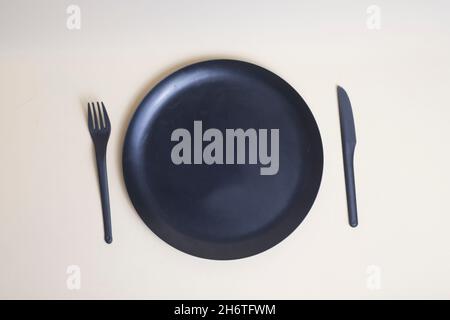 table setting - black plastic knife and fork and black plate isolated on light background flat lay. Image contains copy space Stock Photo