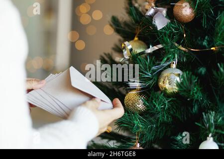 Hand holding stack of craft paper envelopes for christmas greeting card invitation design on christmas tree background with bokeh. Stock Photo
