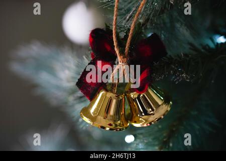 A Christmas decoration with two golden bells and a red ribbon hanging on a Christmas tree Stock Photo