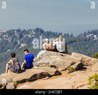 A group of young hikers sitting on a cliff and enjoying the view from the Eagle Bluffs in Cypress Provincial Park, Canada. Concept photo hiking, copy Stock Photo