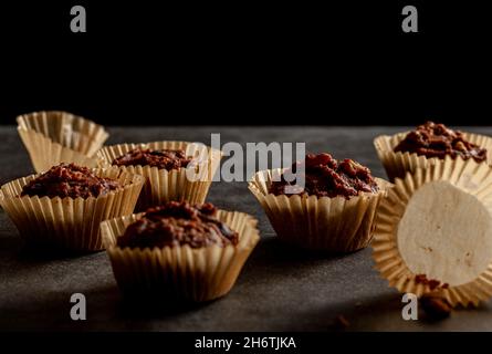 Shallow depth of field angled view of chocolate and nut muffins in liner papers fresh out of oven. Dark background moody low light image. Crumbles on Stock Photo