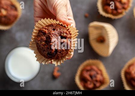 A caucasian woman is holding a fresh baked delicious chocolate nut fresh muffins served on gray background with a glass of milk for dunking. Concept f Stock Photo