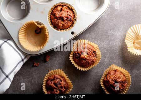 Fruit and nut chocolate cupcakes in liners and nonstick tray served fresh out of oven for breakfast on stone countertop. A cotton cloth is seen by the Stock Photo