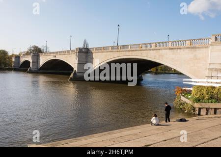 A couple relaxing next to Sir Herbert Baker and Alfred Dryland's Chiswick Bridge on the A316, in Chiswick, west London, England, U.K. Stock Photo