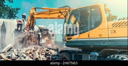 Excavator dismantling house on construction site. Demolition of dilapidated housing for new development. Stock Photo