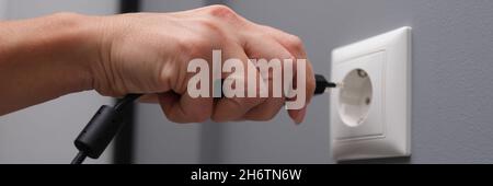 Woman hand inserts electrical plug into outlet closeup Stock Photo
