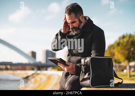Businessman is sitting outdoor in the city and using digital tablet. Stock Photo