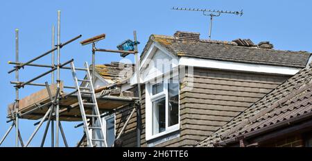 Builders scaffolding tower around dormer rooms for safe ladder access to roof maintenance repair & refit plain roof ridge tiles to house England UK Stock Photo