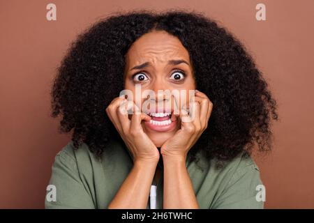 Photo of scared brunette young afro hairstyle lady biting nails wear khaki shirt isolated on brown color background Stock Photo