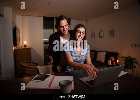 Happy caucasian couple working from home together typing on laptop Stock Photo